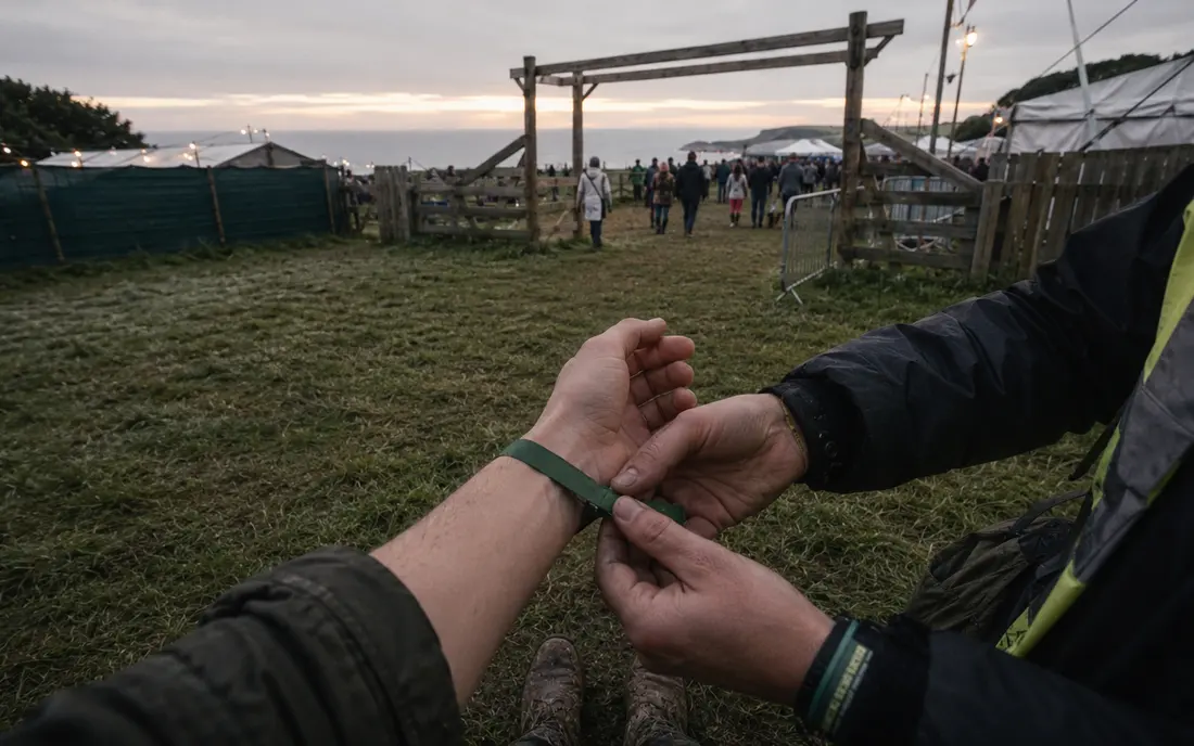 A steward fastening a festival wristband at the gate.